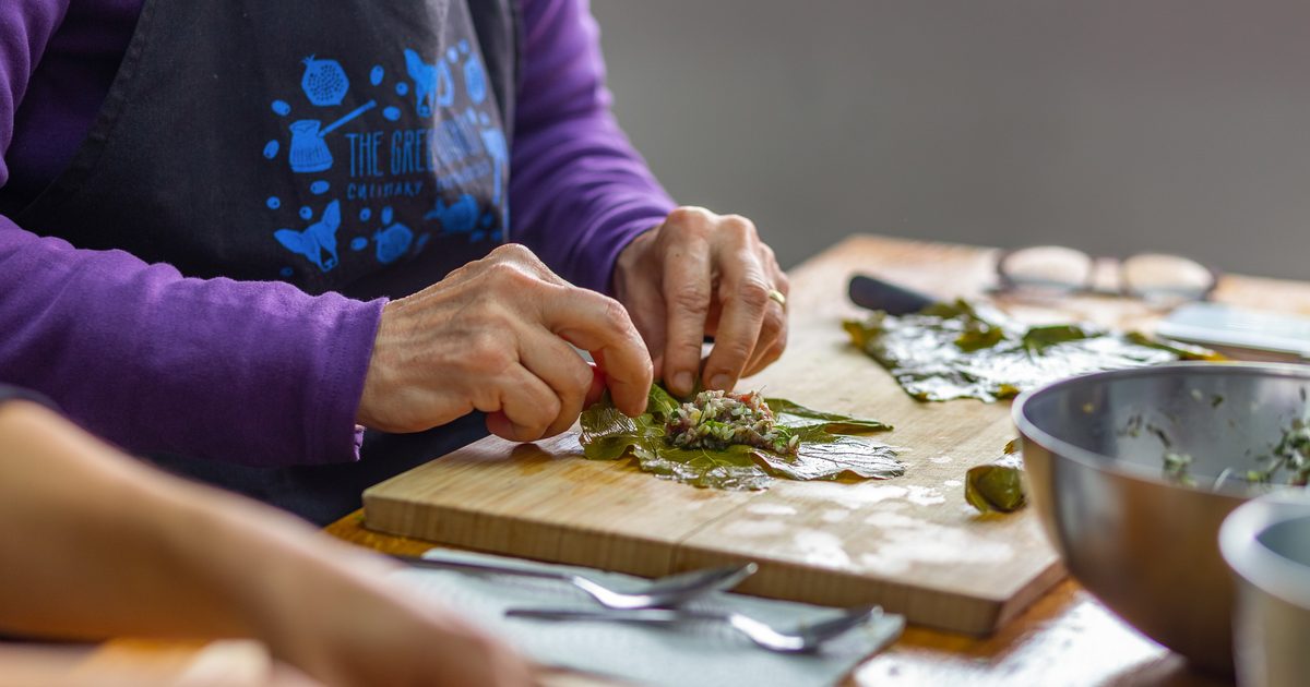 Hands rolling a vine leaf around a rice and herb filling on a wooden board during a cooking class in Athens
