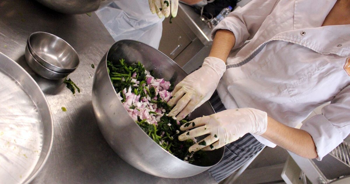 A cook mixing chopped spinach, herbs and red onion in a steel bowl for spanakopita filling